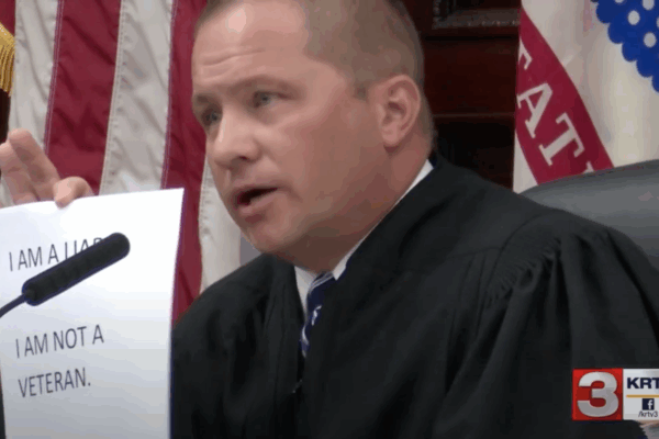 Image of Judge Pinski holding up sign reading I am a liar, I am not a veteran