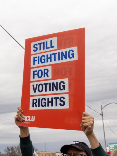 A photo of someone holding an ACLU protest sign that reads 'still fighting for voting rights'