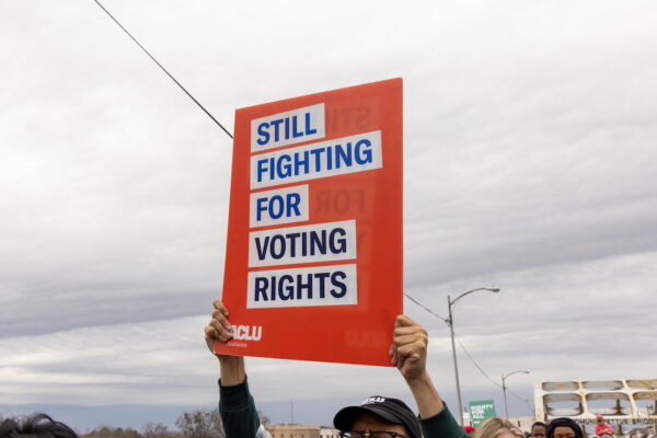 A photo of someone holding an ACLU protest sign that reads 'still fighting for voting rights'