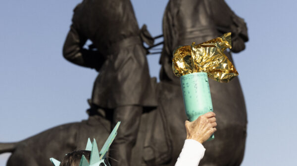 Someone dressed as the Statue of Liberty standing in front of a statue of a man on a horse