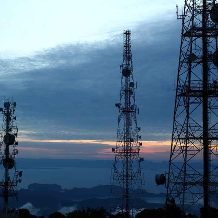 A photo of three cell phone towers in front of a sunset.