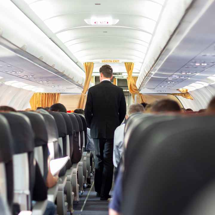 A flight attendant wearing a suit walking through the aisle of a plane.